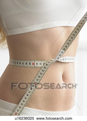 Stock Photography - A measuring tape is twined around a woman' s belly. Fotosearch