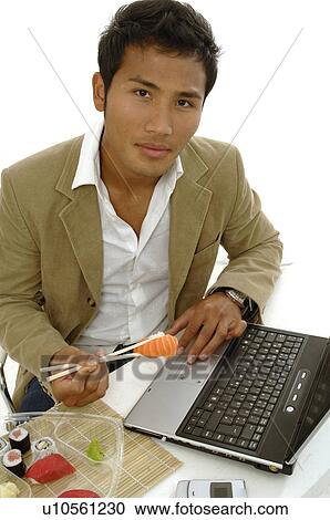Stock Image - Asian man eating sushi at the desk. Fotosearch