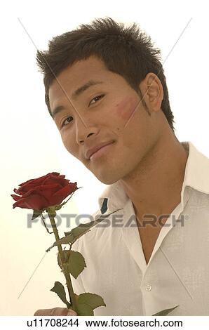 Picture - Asian man with a red rose and kissmouth on his check. Fotosearch