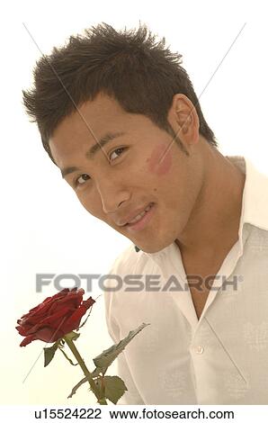 Stock Image - Asian man with a red rose and kissmouth on his check. Fotosearch