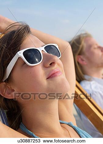 Stock Image - Beautiful young woman with sunglasses taking a sunbath. Fotosearch