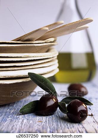 Stock Image - Black olives next to a stack of wooden plates (Olea europaea). Fotosearch