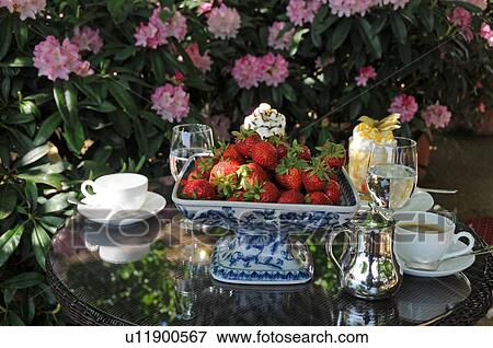 Stock Photo - Bowl with strawberries, coffee and water on outdoor table. Fotosearch