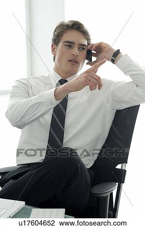 Businessman on phone at desk with laptop pointing with finger View Large Photo Image Stock Image - Businessman on phone at desk with laptop pointing with finger. Fotosearch