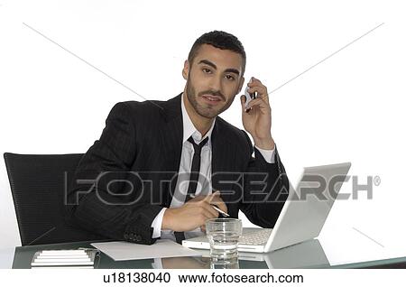 Businessman using cell phone and laptop at desk View Large Photo Image Stock Image - Businessman using cell phone and laptop at desk. Fotosearch