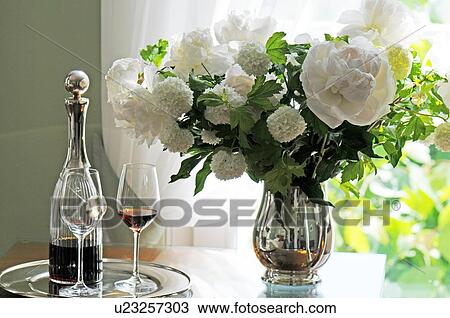 Stock Image - Carafe and bunch of flowers on sideboard. Fotosearch