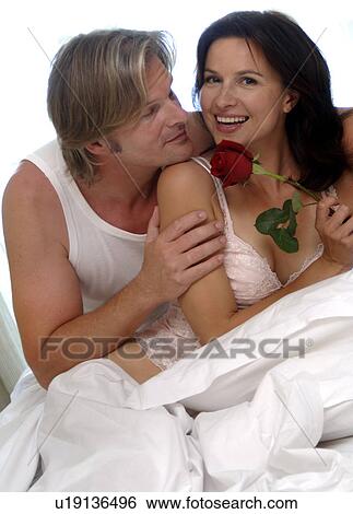 Stock Photograph - Couple in bed, woman is holding a rose. Fotosearch