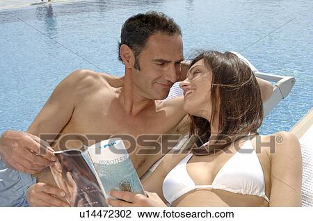 Stock Image - Couple relaxing with a magazine at the swimming pool. Fotosearch