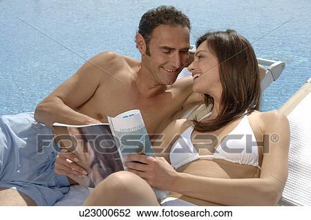 Stock Image - Couple relaxing with a magazine at the swimming pool. Fotosearch