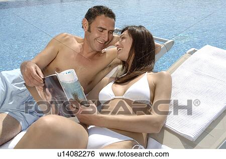 Stock Photograph - Couple relaxing with a magazine at the swimming pool. Fotosearch
