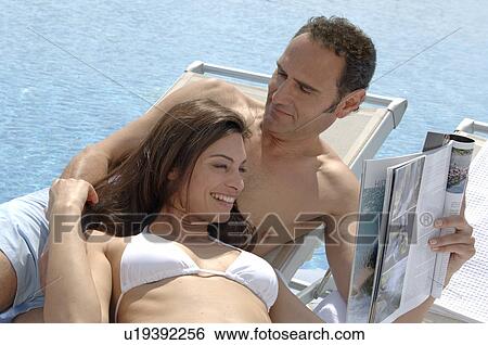 Stock Photograph - Couple relaxing with a magazine at the swimming pool. Fotosearch