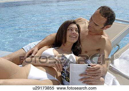 Stock Photography - Couple relaxing with a magazine at the swimming pool. Fotosearch