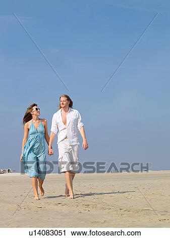 Stock Image - Couple walking hand in hand on the beach. Fotosearch
