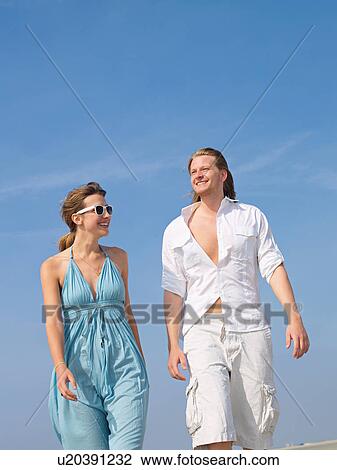 Stock Image - Couple walking hand in hand on the beach. Fotosearch