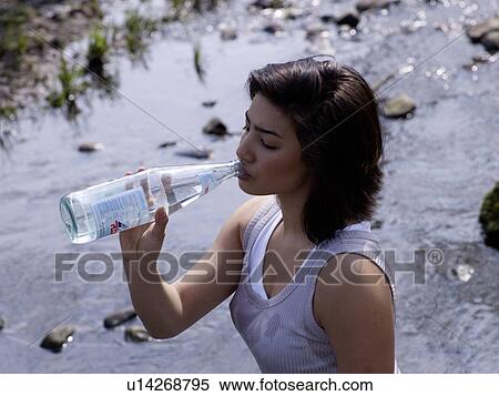 Stock Photography - Dark-haired woman drinking water from bottle. Fotosearch