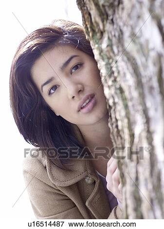 Dark-haired woman looking from behind tree trunk View Large Photo Image Stock Photo - Dark-haired woman looking from behind tree trunk. Fotosearch