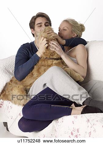 Stock Photo - Man and woman cuddling dog on couch. Fotosearch