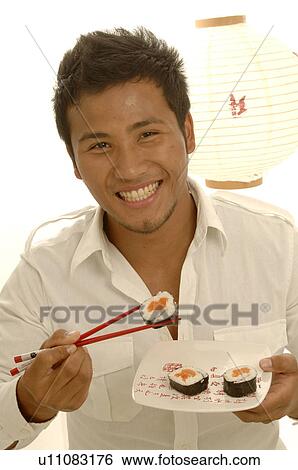 Stock Photograph - Man is eating sushi with chopsticks. Fotosearch