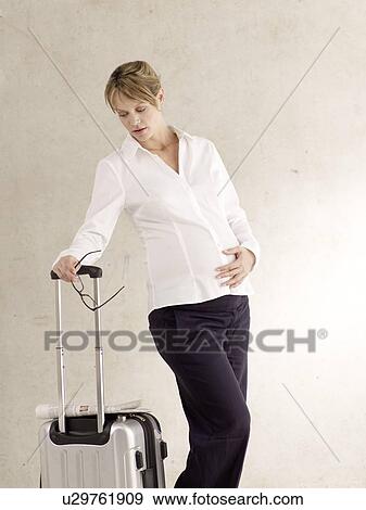 Stock Photo - Pregnant woman with trolley suitcase. Fotosearch