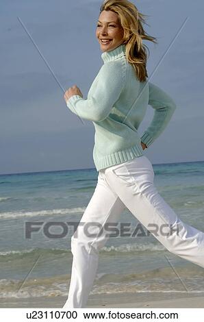Stock Image - Running woman in turquoise pullover at the sea. Fotosearch