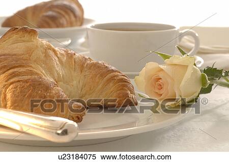 Stock Photography - Table setting with a croissant and a white rose blossom. Fotosearch