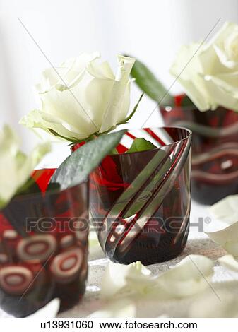 Stock Image - Weiße Rosenblüte in roten Gläsern. Fotosearch