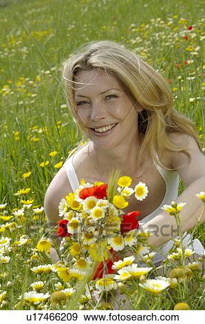 Stock Photo - White dressed women is sitting with a bunch of flowers in a meadow. Fotosearch
