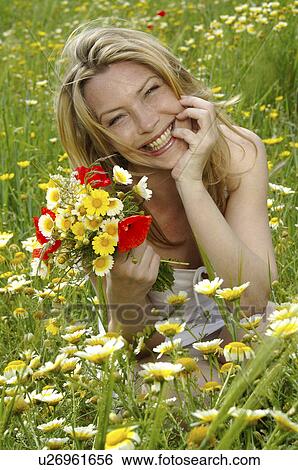 Stock Photograph - White dressed women is sitting with a bunch of flowers in a meadow. Fotosearch