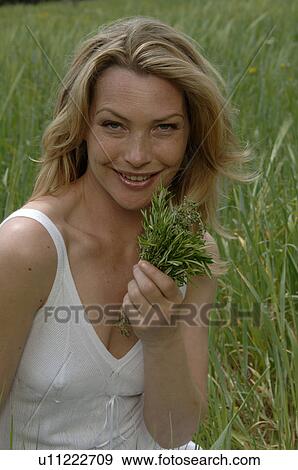 Stock Photo - White dressed women with a bouquet of herbs is sitting in a meadow. Fotosearch