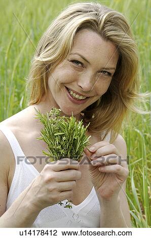 Stock Image - White dressed women with a bunch of weeds is sitting in a meadow. Fotosearch