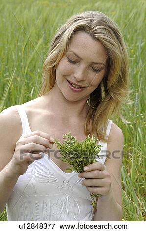 Stock Photo - White dressed women with a bunch of weeds is sitting in a meadow. Fotosearch