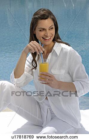 Stock Photo - Woman dressed in white enjoying a drink at the swimming pool. Fotosearch