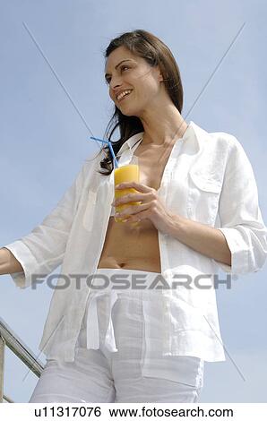 Stock Photograph - Woman dressed in white enjoying a drink at the swimming pool. Fotosearch