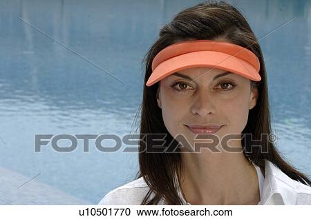 Stock Image - Woman dressed in white with an orange sun shade is sitting at the swimming pool. Fotosearch