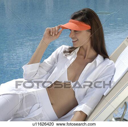 Stock Image - Woman dressed in white with an orange sun shade is sitting at the swimming pool. Fotosearch
