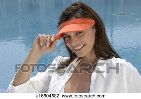 Stock Image - Woman dressed in white with an orange sun shade is sitting at the swimming pool. Fotosearch