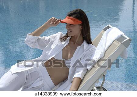 Stock Photo - Woman dressed in white with an orange sun shade is sitting at the swimming pool. Fotosearch