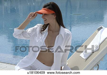 Stock Photo - Woman dressed in white with an orange sun shade is sitting at the swimming pool. Fotosearch