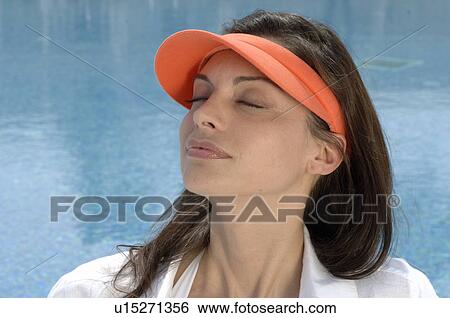 Stock Photograph - Woman dressed in white with an orange sun shade is sitting at the swimming pool. Fotosearch