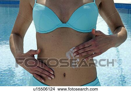 Picture - Woman in a turquoise bikini is applying sunlotion on her belly - at the swimming pool. Fotosearch
