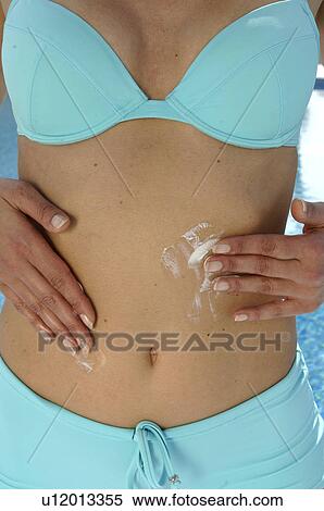 Stock Photography - Woman in a turquoise bikini is applying sunlotion on her belly. Fotosearch