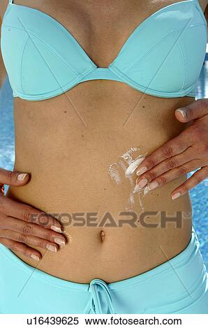 Stock Photography - Woman in a turquoise bikini is applying sunlotion on her belly - at the swimming pool. Fotosearch