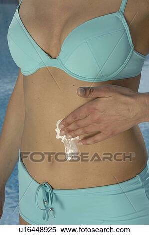 Stock Photography - Woman in a turquoise bikini is applying sunlotion on her belly. Fotosearch