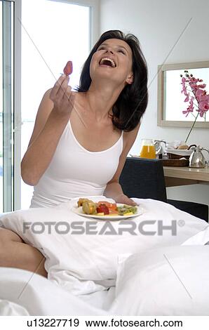 Stock Photo - Woman in bed with fruits on a plate. Fotosearch