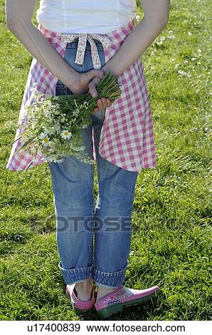 Stock Photo - Woman in garden holding bunch of flowers behind her back. Fotosearch