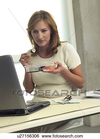 Stock Photograph - Woman is eating sushi at her desk. Fotosearch