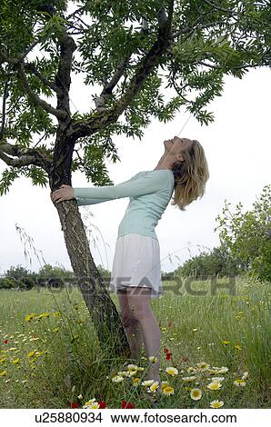 Picture - Woman is embracing a tree in a meadow. Fotosearch