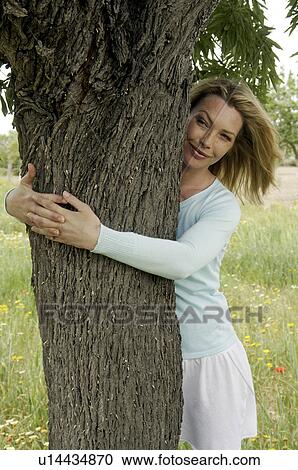 Stock Image - Woman is embracing a tree in a meadow. Fotosearch