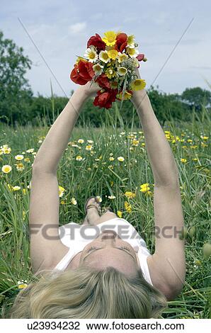 Stock Image - Woman is lying in a meadow and holding a bunch of flowers in the air. Fotosearch