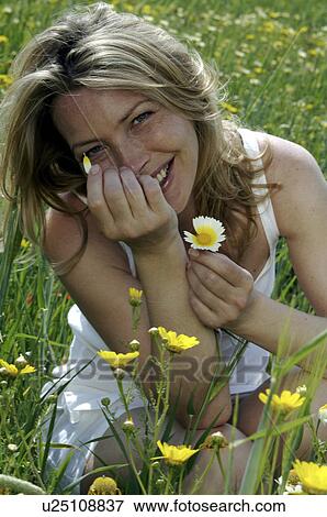 Woman is sitting in a meadow and is playing with a flower View Large Photo Image Stock Photo - Woman is sitting in a meadow and is playing with a flower. Fotosearch